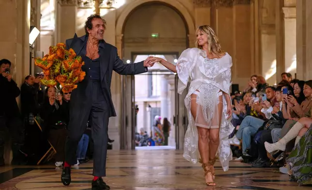 Designer Andreas Kronthaler, left, accepts applause as he holds the hand of Heidi Klum as part of the Vivienne Westwood Spring/Summer 2026 collection presented in Paris, Saturday, Oct. 4, 2025. (AP Photo/Aurelien Morissard)