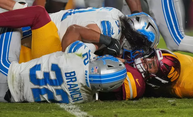 Detroit Lions defensive lineman Roy Lopez, top, and defensive back Brian Branch (32) split a sack of Washington Commanders quarterback Marcus Mariota, right, during the second half of an NFL football game Sunday, Nov. 9, 2025, in Landover, Md. (AP Photo/Stephanie Scarbrough)