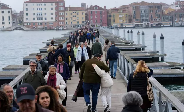 Mourners walk on the 'Votif' Bridge, a 407m temporary floating bridge connecting the city to the cemetery on the island of San Michele, to pay respects to their dead on All Soul's Day, in Venice, Italy, Sunday, Nov. 2, 2025. (AP Photo/Luca Bruno)