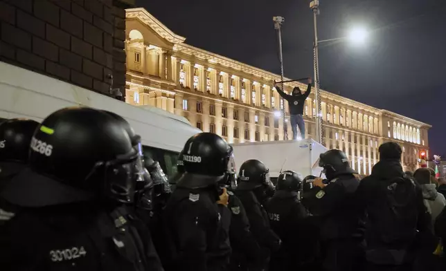 Protester stands on top of a police vehicle as thousands took the streets of Bulgaria's capital, Sofia, to denounce steep tax hikes in next year's draft budget before being finally voted on in parliament, Wednesday, Nov 26, 2025. (AP Photo/Valentina Petrova)