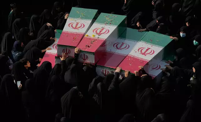 Mourners gather around the flag-draped coffins of unknown Iranian soldiers who were killed in the 1980-88 Iraq-Iran war whose remains were recently recovered from the battlefields, during the funeral ceremony in Tehran, Iran, Monday, Nov. 24, 2025. (AP Photo/Vahid Salemi)