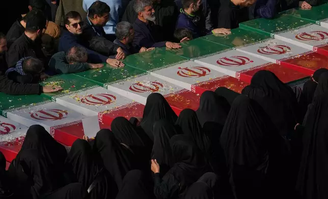 Mourners gather around the flag-draped coffins of unknown Iranian soldiers who were killed in the 1980-88 Iraq-Iran war whose remains were recently recovered from the battlefields, during the funeral ceremony in Tehran, Iran, Monday, Nov. 24, 2025. (AP Photo/Vahid Salemi)