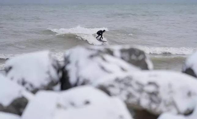 A surfer catches a wave as snow covers the ground n Evanston, Ill., a suburb of Chicago, Monday, Nov. 10, 2025. (AP Photo/Kiichiro Sato)