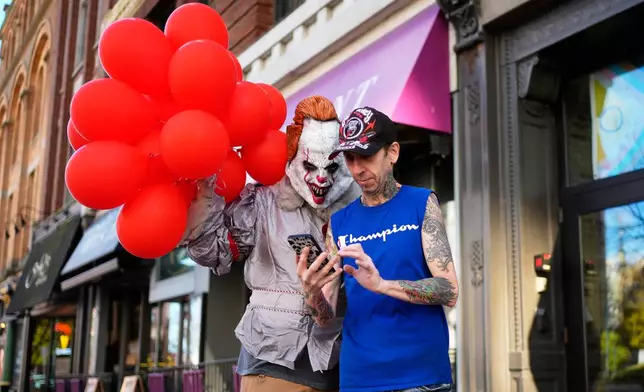 A man dressed as Pennywise, a character from a Steven King novel, checks to see how a selfie turned out with coffee shop worker Jeff Small, Friday, Oct. 31, 2025, in Portland, Maine. (AP Photo/Robert F. Bukaty)