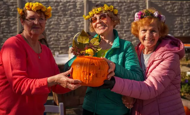 Women pose with a Halloween pumpkin they carved during an event at the Salcetului day care for the elderly state facility in Bucharest, Romania, Friday, Oct. 31, 2025. (AP Photo/Vadim Ghirda)