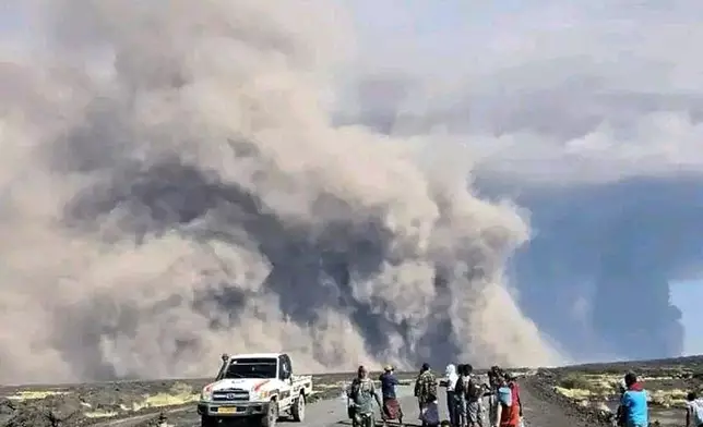 In this photo released by the Afar Government Communication Bureau, people watch ash billow from the first time eruption of the Hayli Gubbi Volcano in Ethiopia's Afar region Sunday, Nov. 23, 2025. (Afar Government Communication Bureau via AP)