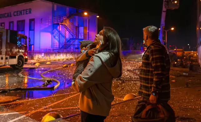 People watch as emergency services personnel work to extinguish a fire following a Russian attack in Kyiv, Ukraine, Tuesday, Nov. 25, 2025. (AP Photo/Dan Bashakov)