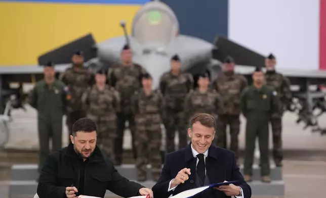 French President Emmanuel Macron, right, and Ukrainian President Volodymyr Zelenskyy sign an agreement Monday, Nov. 17, 2025 at the Villacoublay air base near Paris. (AP Photo/Christophe Ena, Pool)
