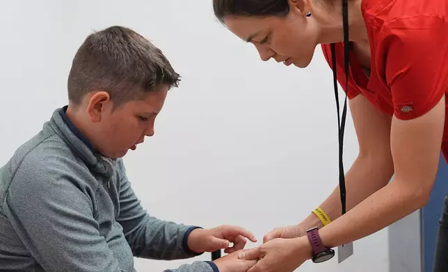 Dr. Natalia Vasquez-Canizares, right, examines Ethan Blanchfield-Killeen, 11, of Yonkers, N.Y., who has a form of juvenile idiopathic arthritis, at the Frost Valley YMCA sleepaway camp in Claryville, N.Y., Thursday, July 31, 2025. The camp partnered with Children's Hospital at Montefiore so kids with autoimmune diseases could attend for the first time. (AP Photo/Matt Rourke)