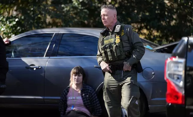 U.S. Border Patrol Commander at large Gregory Bovino, right, looks on as a detainee sits by a car, Monday, Nov. 17, 2025, in Charlotte, N.C. (AP Photo/Matt Kelley)