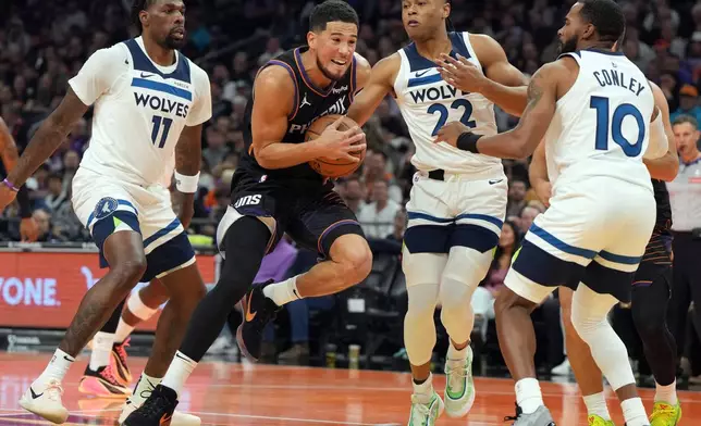 Phoenix Suns guard Devin Booker, second from left, drives between Minnesota Timberwolves center Naz Reid (11), guard Jaylen Clark (22) and guard Mike Conley during the first half of an NBA Cup basketball game, Friday, Nov. 21, 2025, in Phoenix. (AP Photo/Rick Scuteri)