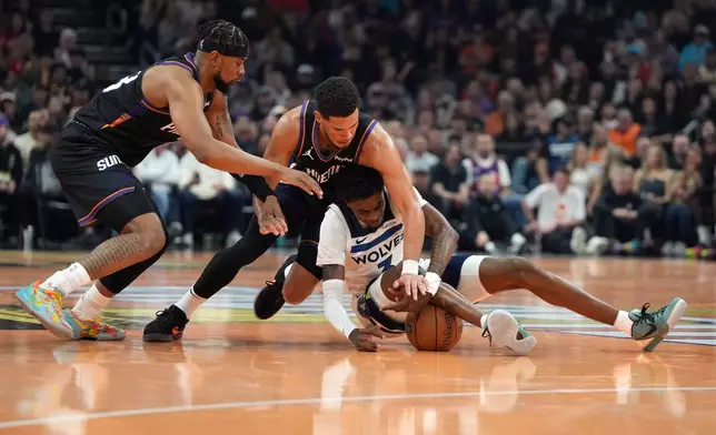 Phoenix Suns guards Jordan Goodwin, left, and Devin Booker, top right, fight for the ball with Minnesota Timberwolves forward Jaden McDaniels, bottom right, during the first half of an NBA basketball game, Friday, Nov. 21, 2025, in Phoenix. (AP Photo/Rick Scuteri)