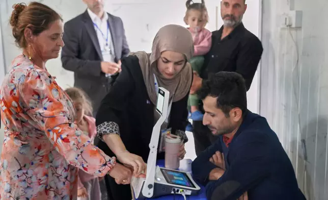 A displaced Yazidi woman has her fingerprint verified before voting ahead of Iraq's parliamentary elections, set for Nov. 11, at a polling station in the Sharia camp near Dohuk, in Iraq's semi-autonomous Kurdish region, Sunday, Nov. 9, 2025. (AP Photo/Rashid Yahya)