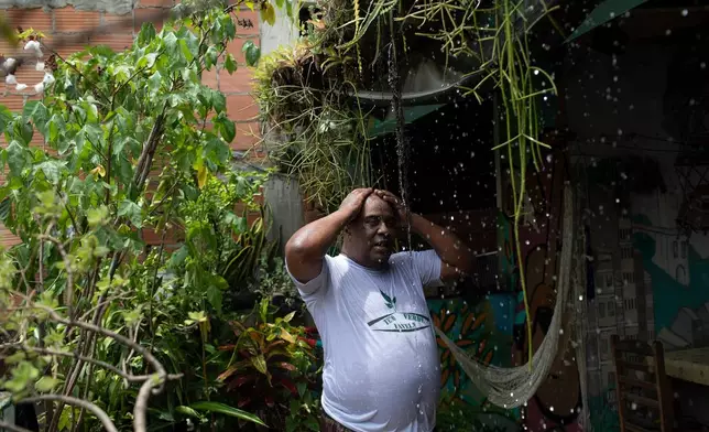 FILE - Luis Cassiano cools off with water that falls from his green roof at his home in Arara, a poor neighborhood, in Rio de Janeiro on Jan. 9, 2020. (AP Photo/Silvia Izquierdo, File)