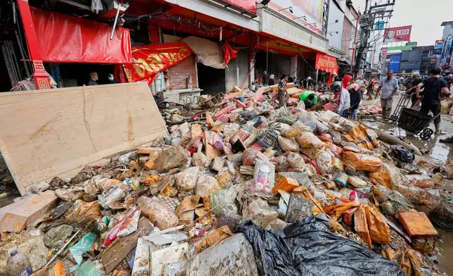 Peoples walk near goods damaged from floods in Songkhla province, southern Thailand, Saturday, Nov. 29, 2025. (AP Photo/Sarot Meksophawannakul)