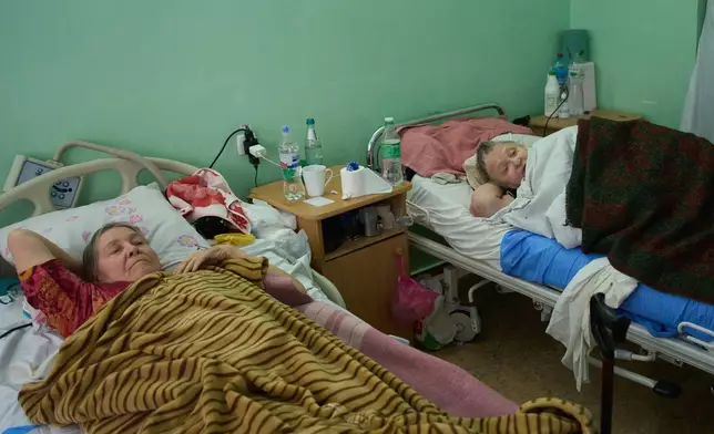 Nataliia Naumova, 70, right, recovers after a Shahed drone blasted her left leg at one of the city main hospitals treating drone victims in the frontline city of Kherson, Southern Ukraine, Monday, Nov. 3, 2025. (AP Photo/Efrem Lukatsky)