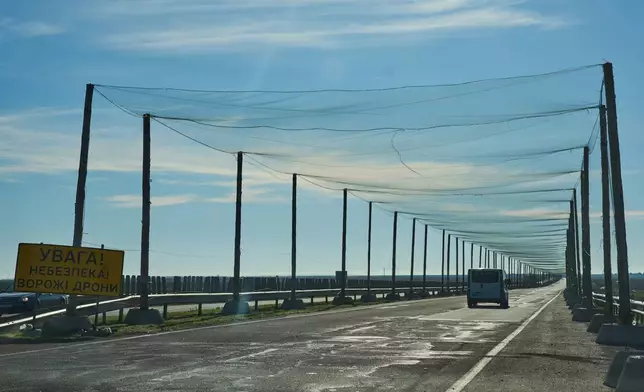 A car drives on a road covered with an anti-FPV-drone net, a road sign reading "Attention/Danger/Enemy drones", at the approaches to the frontline city of Kherson, Southern Ukraine, Sunday, Nov. 2, 2025. (AP Photo/Efrem Lukatsky)