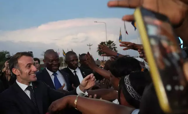 French President Emmanuel Macron, left, and Gabon's President Brice Oligui Nguema shake hands with local people at the Leon-Mba International Airport in Libreville, Gabon, Sunday, Nov. 23, 2025. (AP Photo/Thibault Camus)