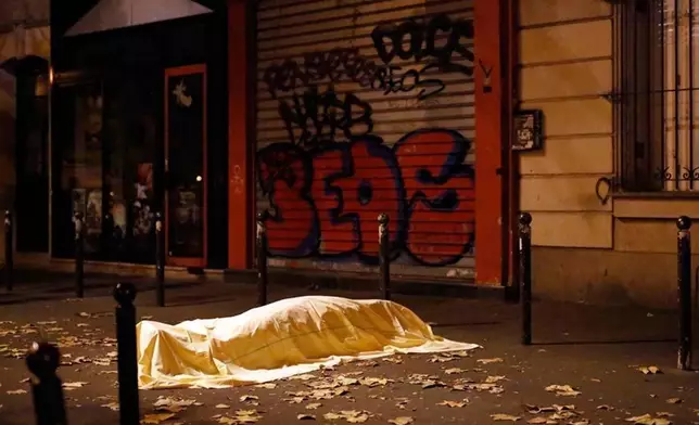 FILE - A victim under a blanket lays dead outside the Bataclan theater in Paris, Nov. 13, 2015. (AP Photo/Jerome Delay, File)
