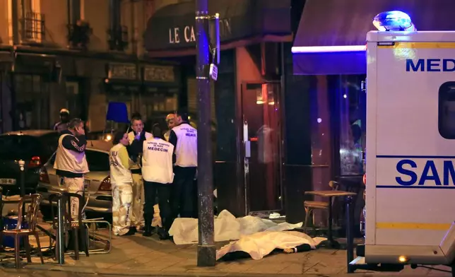FILE - Medics attend the scene as victims lay on the pavement outside a Paris restaurant, Friday, Nov. 13, 2015. (AP Photo/Thibault Camus, File)