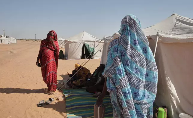 Nadra Mohamed Ahmed, left, stands outside her tent at the newly established El-Afadh camp in Al Dabbah, Sudan's northern state, Monday, Nov. 17, 2025. (AP Photo/Marwan Ali)