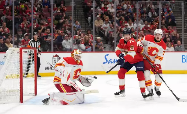 Calgary Flames goaltender Devin Cooley (1) stops a shot as Florida Panthers center Jesper Boqvist (70) and Calgary Flames defenseman Yan Kuznetsov (37) look on, during the second period of an NHL hockey game, Friday, Nov. 28, 2025, in Sunrise, Fla. (AP Photo/Rebecca Blackwell)