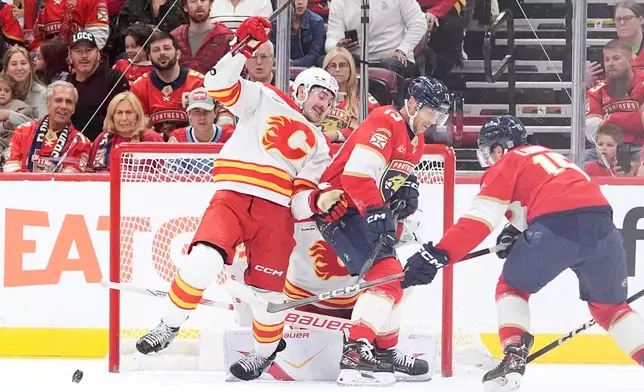 Florida Panthers center Anton Lundell, right, and center Sam Reinhart attempt to score as Calgary Flames defenseman Brayden Pachal, left, and goaltender Devin Cooley, obscured, defend during the first period of an NHL hockey game, Friday, Nov. 28, 2025, in Sunrise, Fla. (AP Photo/Rebecca Blackwell)