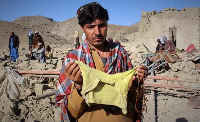 A man shows children's clothing, allegedly belonging to a victim, as locals search through the rubble at the site of an overnight attack on a home that, according to an Afghan government spokesman, was carried out by Pakistan, in the Gurbaz district of Khost province, Afghanistan, Tuesday, Nov. 25, 2025. (AP Photo/Saifullah Zahir)