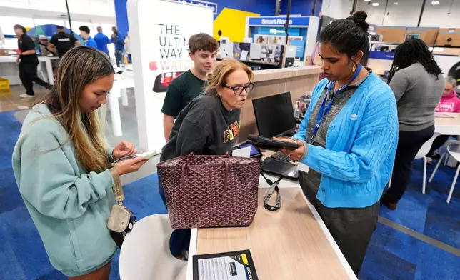Yugita Suresh, right, an AT&amp;T account representative assists Patricia Neerman and her children Jonathan, right rear, and Esther, left, through a purchase at Best Buy, Wednesday, Nov. 26, 2025, in Dallas. (AP Photo/Tony Gutierrez)