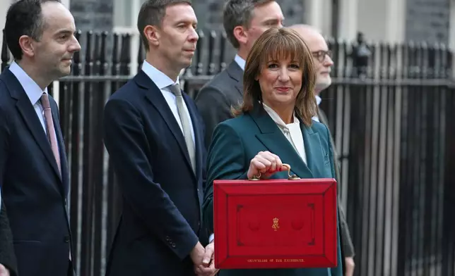 Britain's Chancellor of the Exchequer Rachel Reeves hold up her ministerial red box as she poses with members of her Treasury team on the doorstep of 11 Downing Street,before heading to the House of Commons to deliver her Budget speech in London, Wednesday, Nov. 26, 2025.(AP Photo/Thomas Krych)