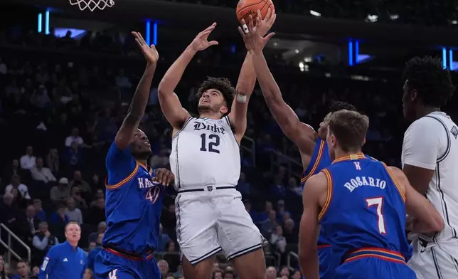 Duke's Cameron Boozer (12) drives past Kansas' Flory Bidunga (40) and Kohl Rosario (7) during the first half of an NCAA college basketball game Tuesday, Nov. 18, 2025, in New York. (AP Photo/Frank Franklin II)