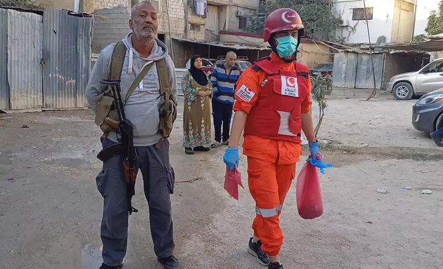 A Hamas gunman, left, stands next of a Palestinian rescue man who carries a bag with body remains, near the scene where an Israeli strike hit on Tuesday night the Ein el-Hilweh Palestinian refugee camp, in the southern port city of Sidon, Lebanon, Wednesday, Nov. 19, 2025. (AP Photo/Mohammed Zaatari)