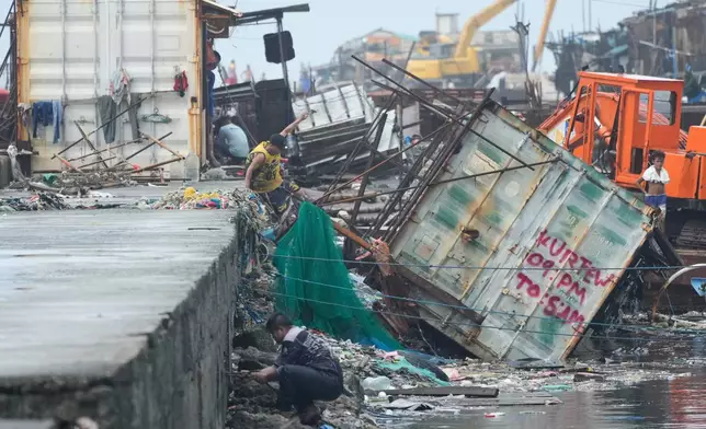 A man jumps beside a container van that was toppled due to Typhoon Fung-wong on Monday, Nov. 10, 2025, in Navotas, Philippines. (AP Photo/Aaron Favila)