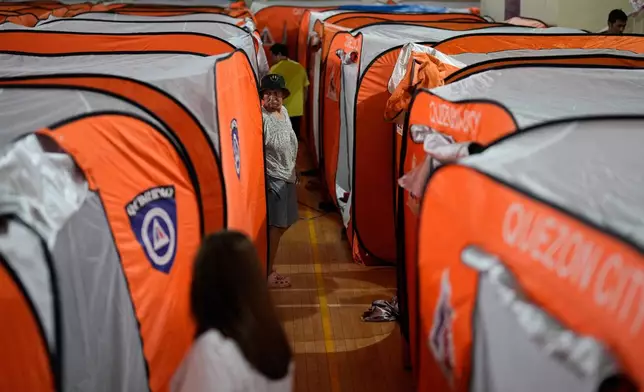 A woman walks beside tents at an evacuation center as Typhoon Fung-wong enters the country on Sunday, Nov. 9, 2025 in Quezon city, Philippines. (AP Photo/Aaron Favila)
