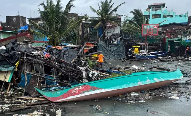 A man walks beside a damaged house and boat due to Typhoon Fung-wong along a coastal village on Monday, Nov. 10, 2025, in Navotas, Philippines. (AP Photo/Aaron Favila)