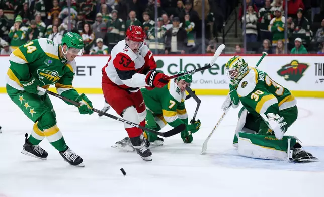 Carolina Hurricanes right wing Jackson Blake (53) and Minnesota Wild center Joel Eriksson Ek (14) compete for the puck as goaltender Jesper Wallstedt (30) defends his net during overtime of an NHL hockey game Wednesday, Nov. 19, 2025, in St. Paul, Minn. (AP Photo/Matt Krohn)