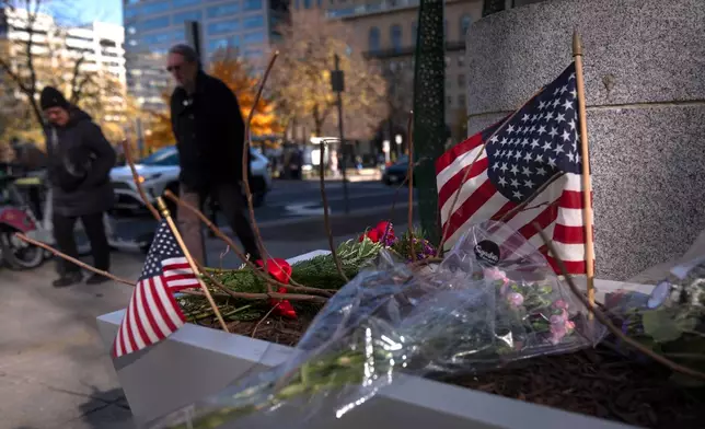 People walk past a small memorial in a planter, Friday, Nov. 28, 2025, near the site where two National Guard members were shot in Washington. (AP Photo/Mark Schiefelbein)