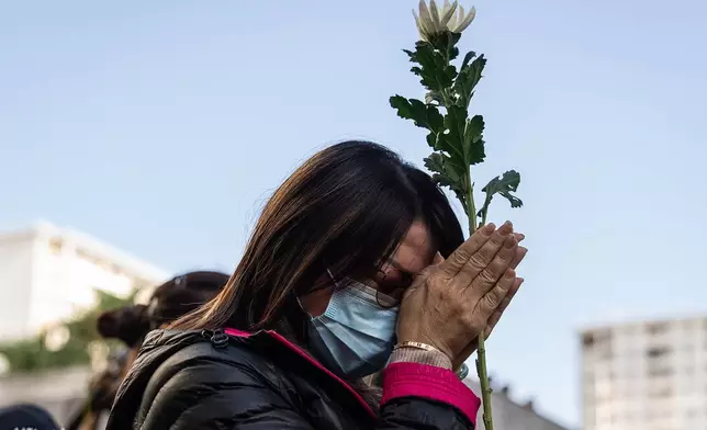 People holds flower and prays near the scene after the deadly fire that started Wednesday at Wang Fuk Court, a residential estate in the Tai Po district of Hong Kong's New Territories, Saturday Nov. 29, 2025. (AP Photo/Chan Long Hei)