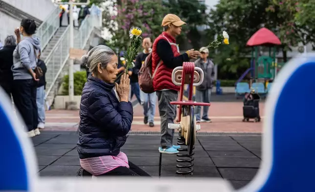 People holds flowers and prays near the scene after the deadly fire that started Wednesday at Wang Fuk Court, a residential estate in the Tai Po district of Hong Kong's New Territories, Saturday Nov. 29, 2025. (AP Photo/Chan Long Hei)