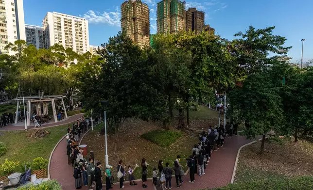 People holds flower and line up near the site to mourn the victims of the deadly Wednesday fire at Wang Fuk Court, a residential estate in the Tai Po district of Hong Kong's New Territories on Saturday, Nov. 29, 2025. (AP Photo/Chan Long Hei)