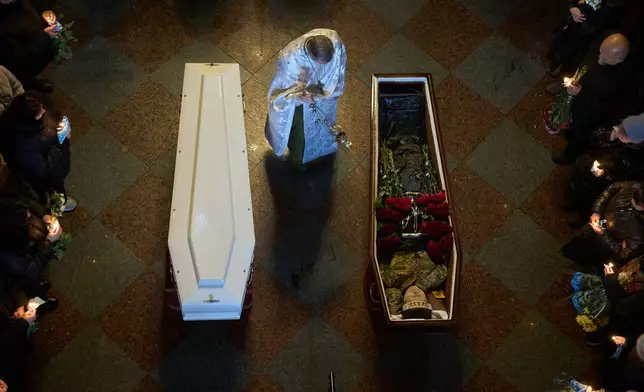 A priest conducts a service as people say the last goodbye to Ukrainian soldiers Myroslava Kopcha and Artur Vilchynski, who were killed in Russia-Ukraine war, during a funeral ceremony at St. Michael Cathedral in Kyiv, Ukraine, Friday, Nov. 28, 2025. (AP Photo/Efrem Lukatsky)
