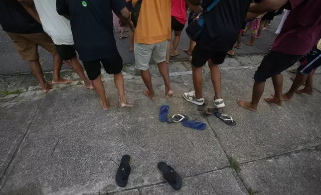 Sandals sit on the sidewalk as Indigenous peoples sing and dance as they participate in an opening ceremony as part of the People's Summit offsite from the COP30 U.N. Climate Summit, Wednesday, Nov. 12, 2025, in Belem, Brazil. (AP Photo/Fernando Llano)