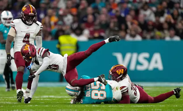 Washington Commanders cornerback Mike Sainristil (0) flies through the air after assisting with a tackle on Miami Dolphins tight end Greg Dulcich (85) during the first half of an NFL football game between the Washington Commanders and the Miami Dolphins in Madrid, Spain, Sunday, Nov. 16, 2025. (AP Photo/Bernat Armangue)