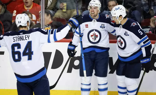 Winnipeg Jets' Tanner Pearson (70) celebrates his goal with teammates Logan Stanley (64) and Luke Schenn during second period NHL hockey action against the Calgary Flames, in Calgary, Alta., Saturday, Nov. 15, 2025. (Jeff McIntosh/The Canadian Press via AP)