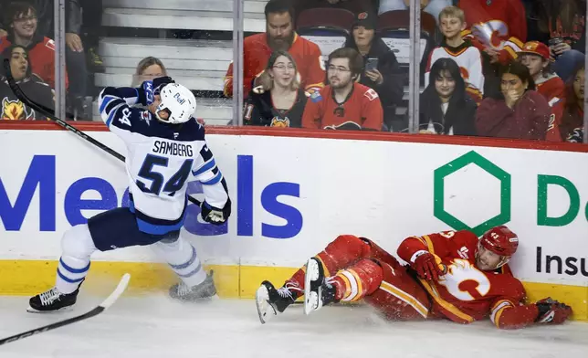 Winnipeg Jets' Dylan Samberg (54) checks Calgary Flames' Adam Klapka during the first period of an NHL hockey game in Calgary, Alberta, Saturday, Nov. 15, 2025. (Jeff McIntosh/The Canadian Press via AP)