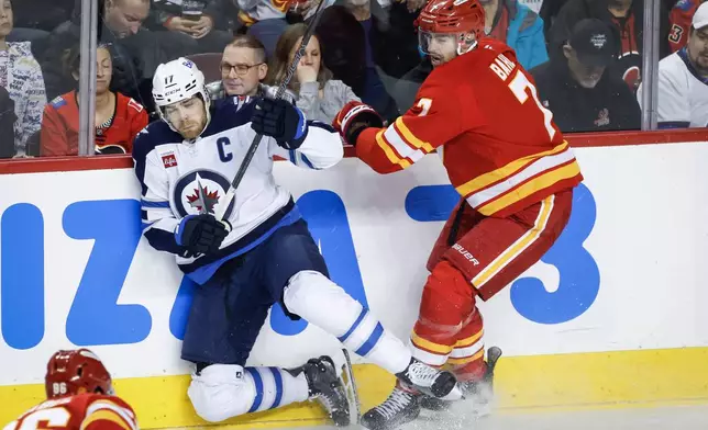Winnipeg Jets' Adam Lowry (17) is checked by Calgary Flames' Kevin Bahl during the first period of an NHL hockey game in Calgary, Alberta, Saturday, Nov. 15, 2025. (Jeff McIntosh/The Canadian Press via AP)