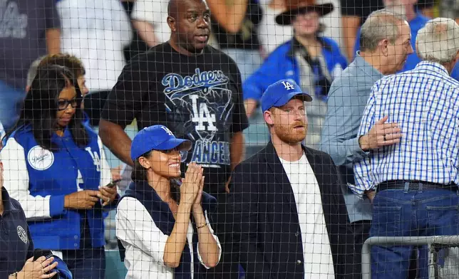 Prince Harry, right, and Meghan Markle, left, The Duke and Duchess of Sussex, and Magic Johnson, back, watch during the seventh inning in Game 4 of baseball's World Series between the Los Angeles Dodgers and the Toronto Blue Jays in Los Angeles, Tuesday, Oct. 28, 2025. (Frank Gunn/The Canadian Press via AP)