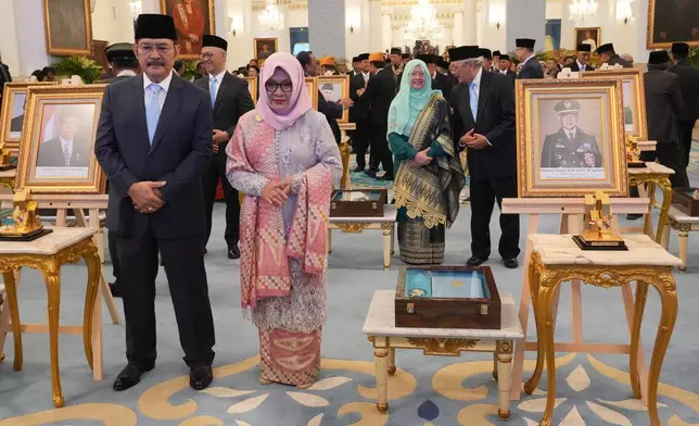 Siti Hardiyanti Rukmana, second left, daughter of the late President Suharto and son Bambang Trihatmojo, left, pose for photographers next to the portrait of their father during a ceremony awarding national hero title to ten figures including the former strongman, at the State Palace in Jakarta, Indonesia, Monday, Nov. 10, 2025. (AP Photo/Achmad Ibrahim)
