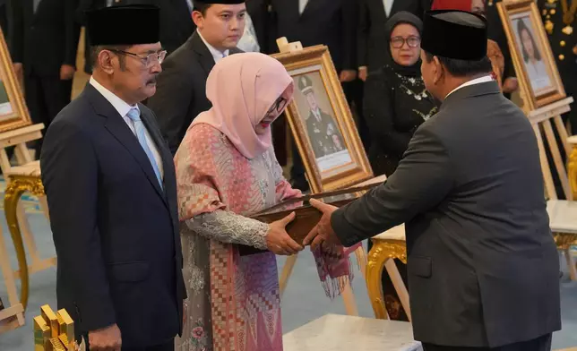 Indonesian President Prabowo Subianto, right, hands a national hero certificate to Siti Hardiyanti Rukmana, second left, daughter of the late President Suharto and son Bambang Trihatmojo, left, during a ceremony awarding national hero title to ten figures including the former strongman, at the State Palace in Jakarta, Indonesia, Monday, Nov. 10, 2025. (AP Photo/Achmad Ibrahim)