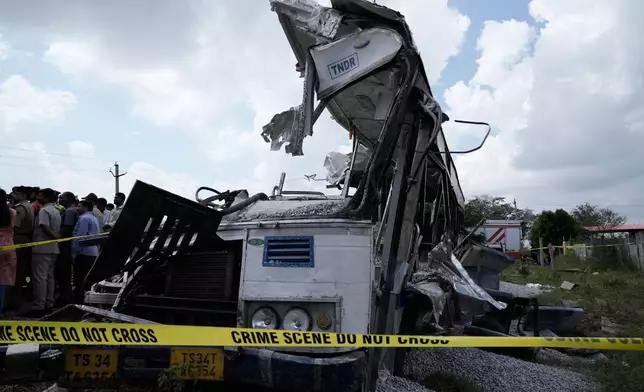 CAPTION CORRECTS THE LOCATION - People stand next to the passenger bus after a truck loaded with concrete stone chips rammed into it at Chevella in southern state of Telangana, India, Monday, Nov. 3, 2025. (AP Photo/Mahesh Kumar A.)